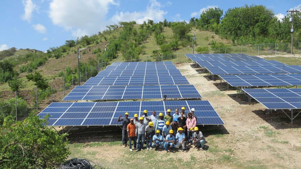 A group of solar technicians pose for a photo in front of a large field of solar panels