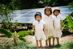 Three children in Colombia stand in front of their community's new solar panels