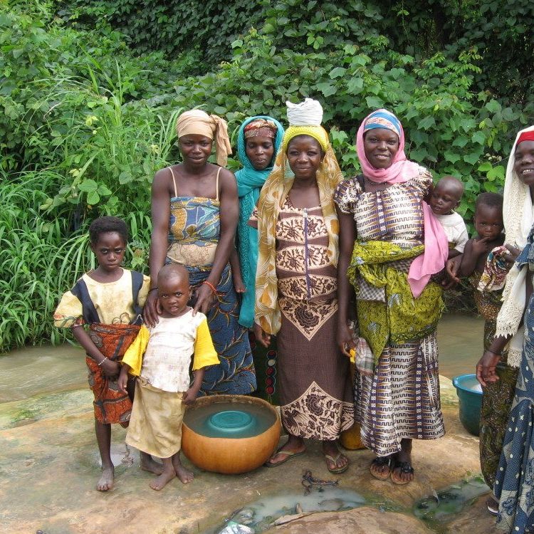 Women and children smile for a photo by a small creek