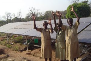 Three girls celebrate in front of their community's new solar panels