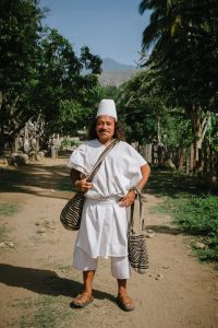 An Arhuaco man stands along a dirt path surrounded by trees