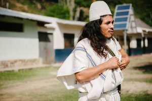 An Arhuaco man stands in front of a solar-powered community building