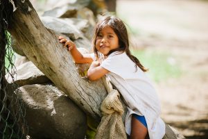 A child leans against a tree branch and stones in an Arhuaco community