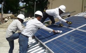 Three technicians install solar panels at College Marie Reine Immaculée in Port-au-Prince, Haiti