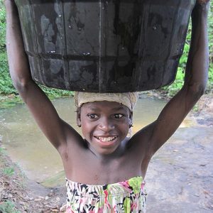 A young girl in Benin holds a large bucket of water on her head