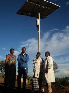 Medical staff and others stand under a solar panel that generates power for their clinic