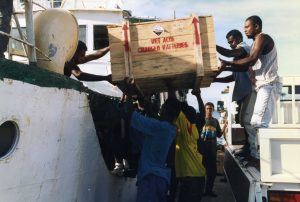 A group of men unload a box of batteries from a ship in the Solomon Islands