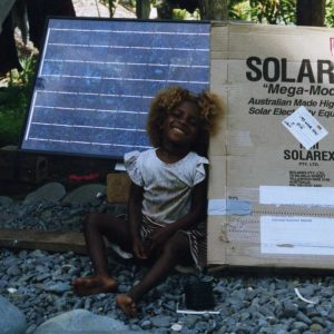 A child smiles next to a solar panel that will provide power to her community