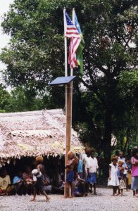 People stand beneath a flag pole with flags from the United States and the Solomon Islands