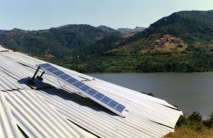 A solar panel sits on a tin rooftop by a lake