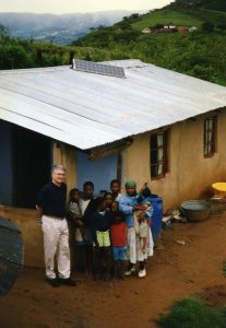 People stand outside of a small home with a rooftop solar panel