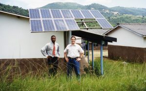 Two men stand in front of a solar array that delivers energy to a school