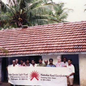 People hold up a Solar Electric Light Fund (SELF) banner outside a community building in Sri Lanka