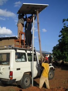 Group of men work to set up a solar panel on a tall pole in Tanzania