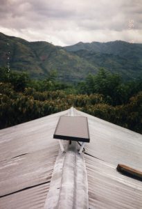 A solar panel sits on a rooftop against a mountain landscape in Uganda