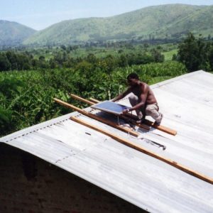 A person attaches a solar panel to a rooftop in Uganda