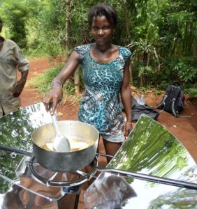 A woman cooks food over a reflective solar cooking appliance