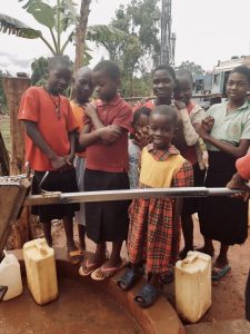 Children smile next to a clean water pump