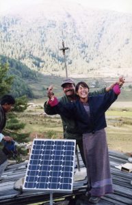 Two people celebrate a new solar panel installed on a rooftop in Bhutan