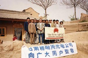 People with a Solar Electric Light Fund (SELF) flag pose for a photo outside a building in China