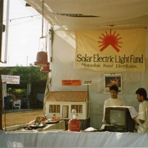 Two people stand in a booth with Solar Electric Light Fund signs in India