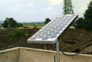 A photovoltaic panel stands against the backdrop of a community in rural India