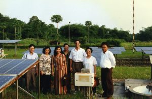 Group of people stand smiling in a field with solar panels