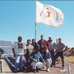People stand in front of solar panels with a flag on Navajo land