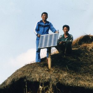 Two people in Nepal smile from a rooftop next to their new solar panel