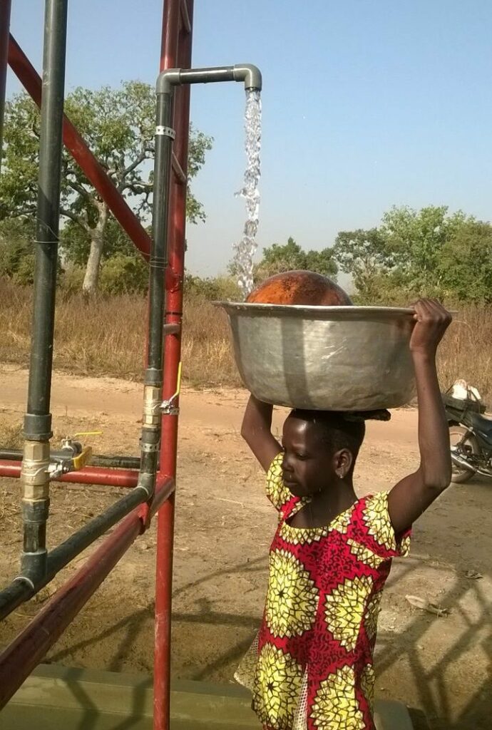 A child in Benin stands under a clean water pump, which is powered by solar energy