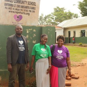 Three people stand outside the Kamuli Community School in Bukyerimba, Uganda