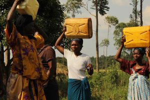 Women experiencing energy poverty carry containers of water on their heads from a local lake to their village