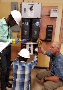 An instructor trains two technicians on how to install an inverter for a solar energy system