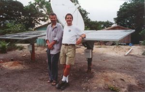 Two people lean against a solar panel, which powers a rural community in Brazil