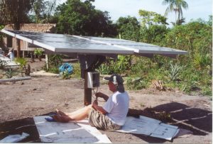 A solar engineer sets up a solar array in Brazil, surrounded by the jungle and thatched roof building