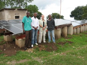 Doctors and solar technicians stand in front of a solar array at a health clinic in Burundi