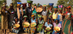Group of women smile with produce grown in their Solar Market Garden