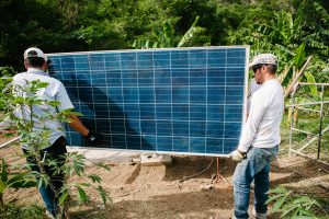 Two technicians carry a solar panel to be installed in Colombia