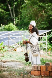 Arhuaco man stands in front of new solar panels installed by the Solar Electric Light Fund (SELF)