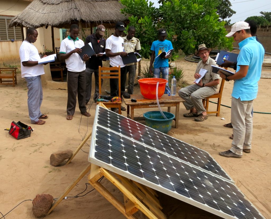 Group of men at a Solar Electric Light Fund (SELF) project site review technical details for solar panels at a sustainable development project site