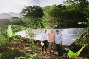 Three men stand in front of a solar panel. Solar energy provides solutions to energy poverty.